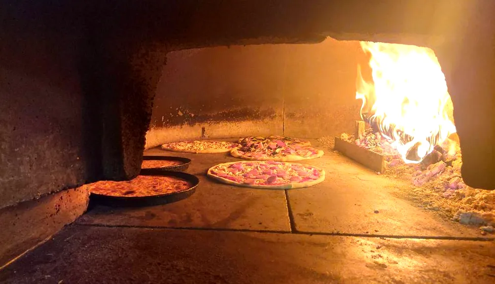 Due pizze che cuociono sulla pietra del forno a legna, con la fiamma accesa sul fondo