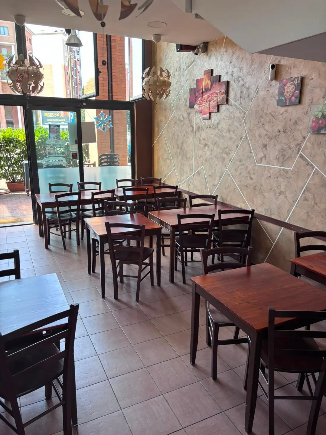 La sala della pizzeria al piano terra: tavoli e sedie in legno scuro, grandi vetrate sulla strada